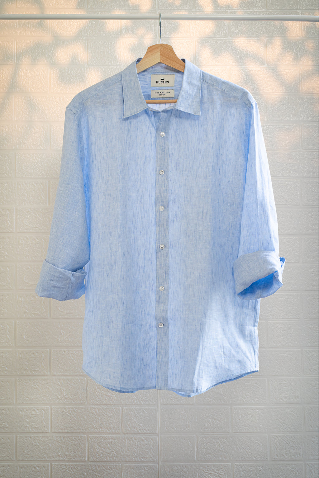 Ocean / Light blue striped shirt on a hanger against a light tiled wall.