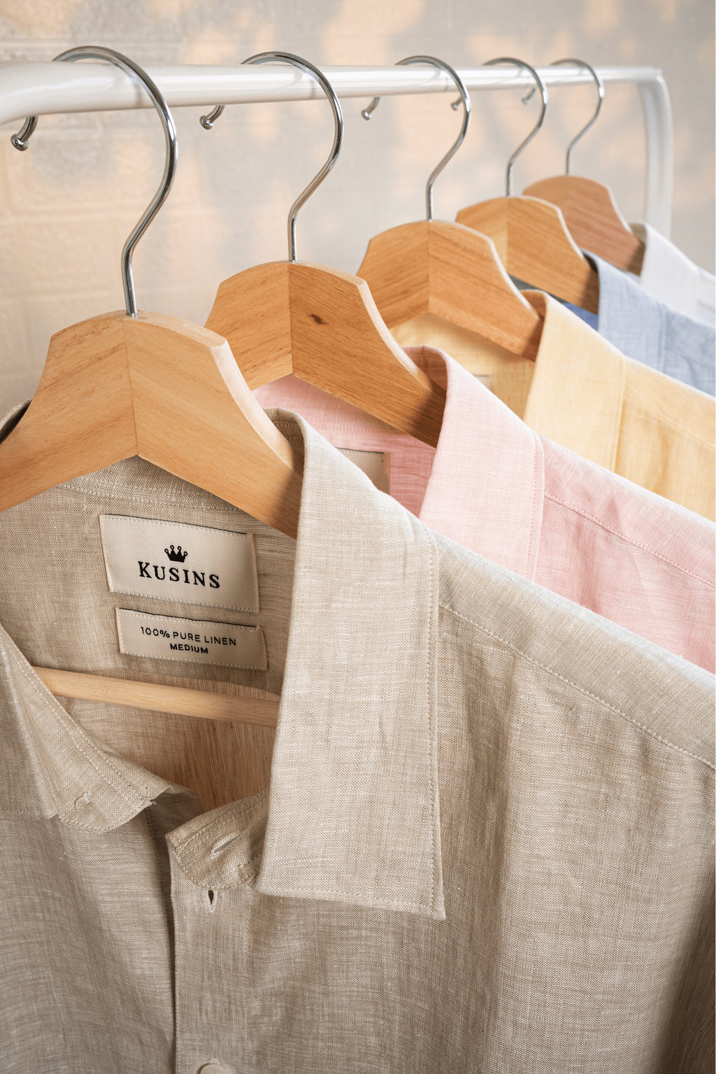 Sand shirt in front of other Shirts hanging on wooden hangers with visible brand labels.