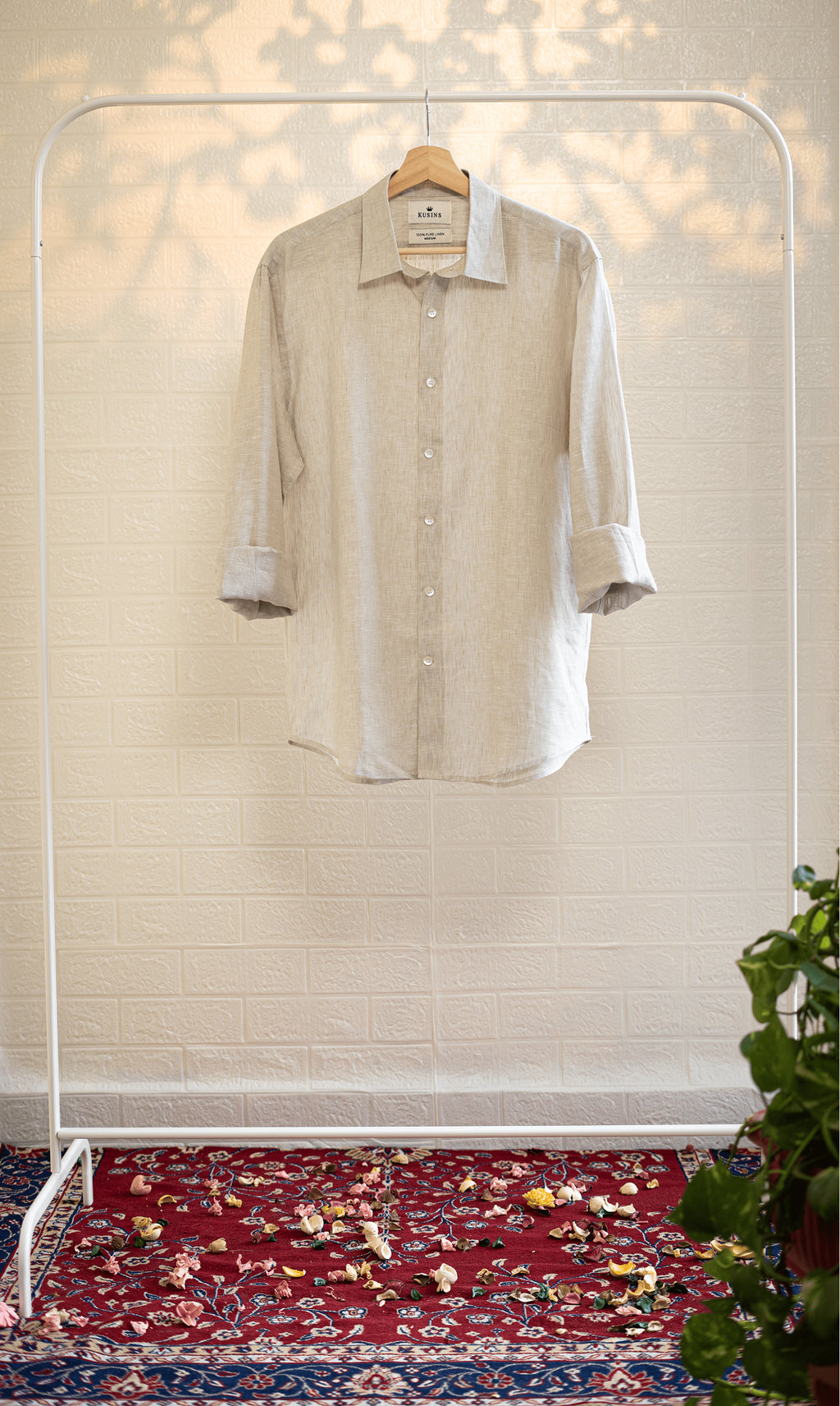 Sand / Beige shirt on a hanger against a white wall with a patterned rug at the bottom.