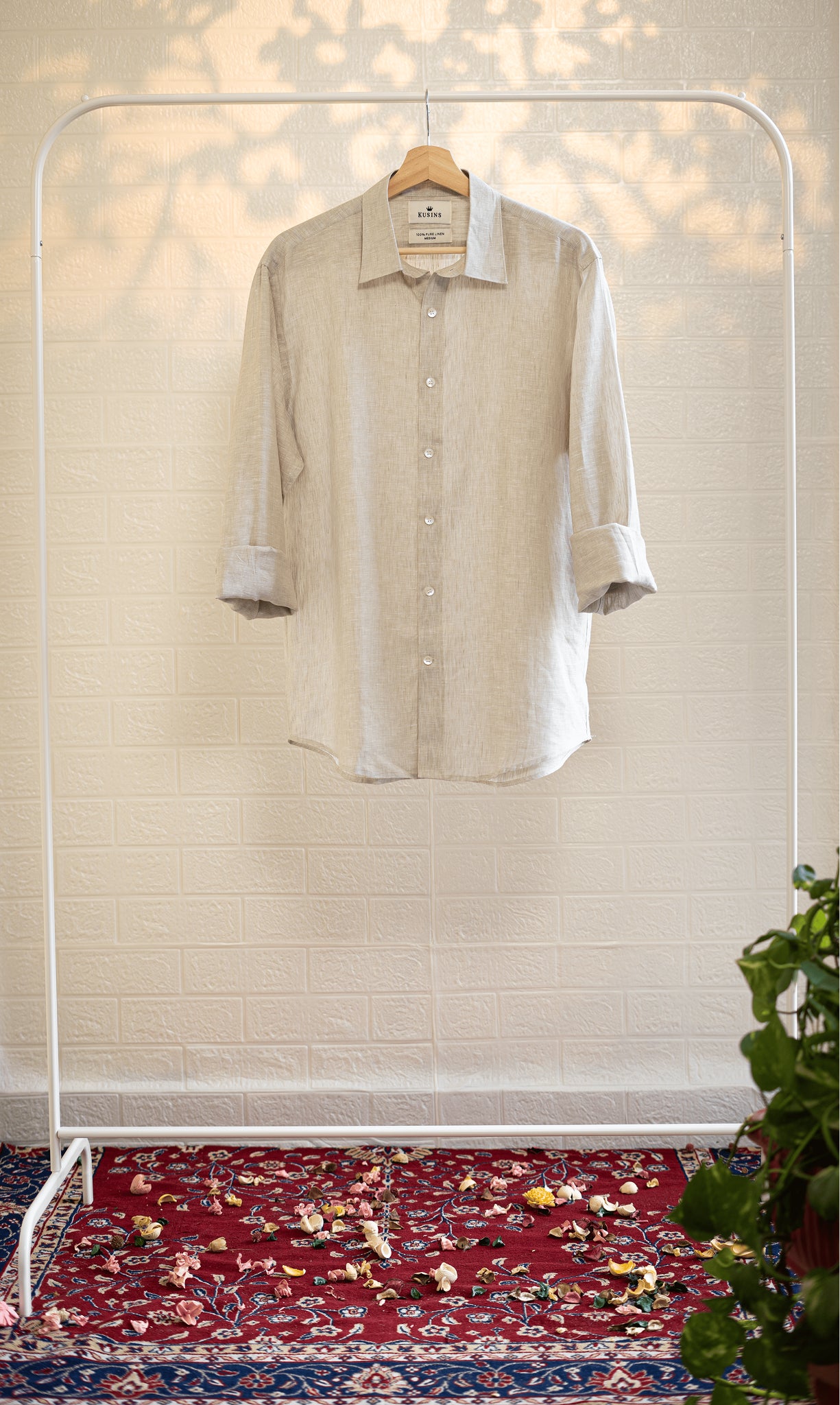 Sand / Beige shirt on a hanger against a white wall with a patterned rug at the bottom.