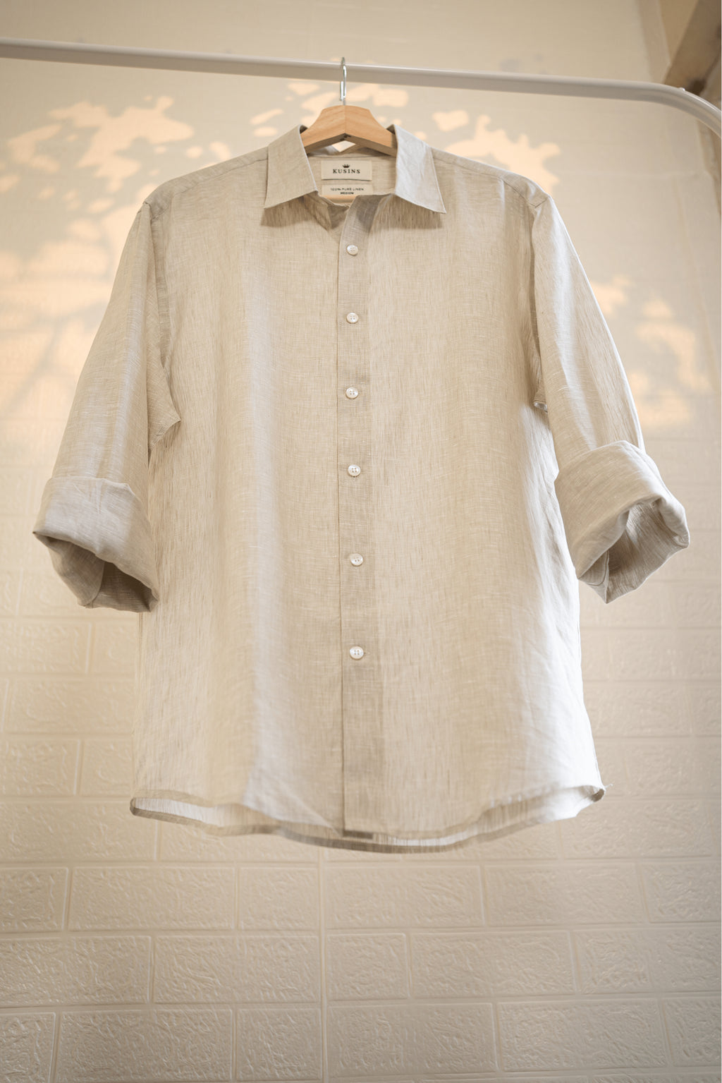 Sand / Beige shirt on a hanger against a light-colored wall