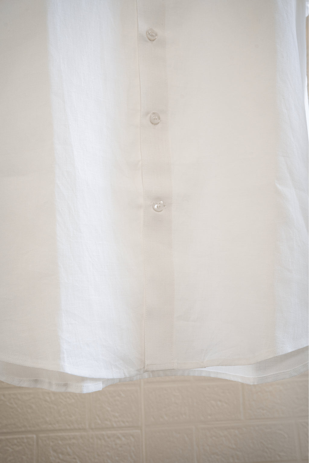 Close-up of a  chalk or white button-up shirt with a textured beige background
