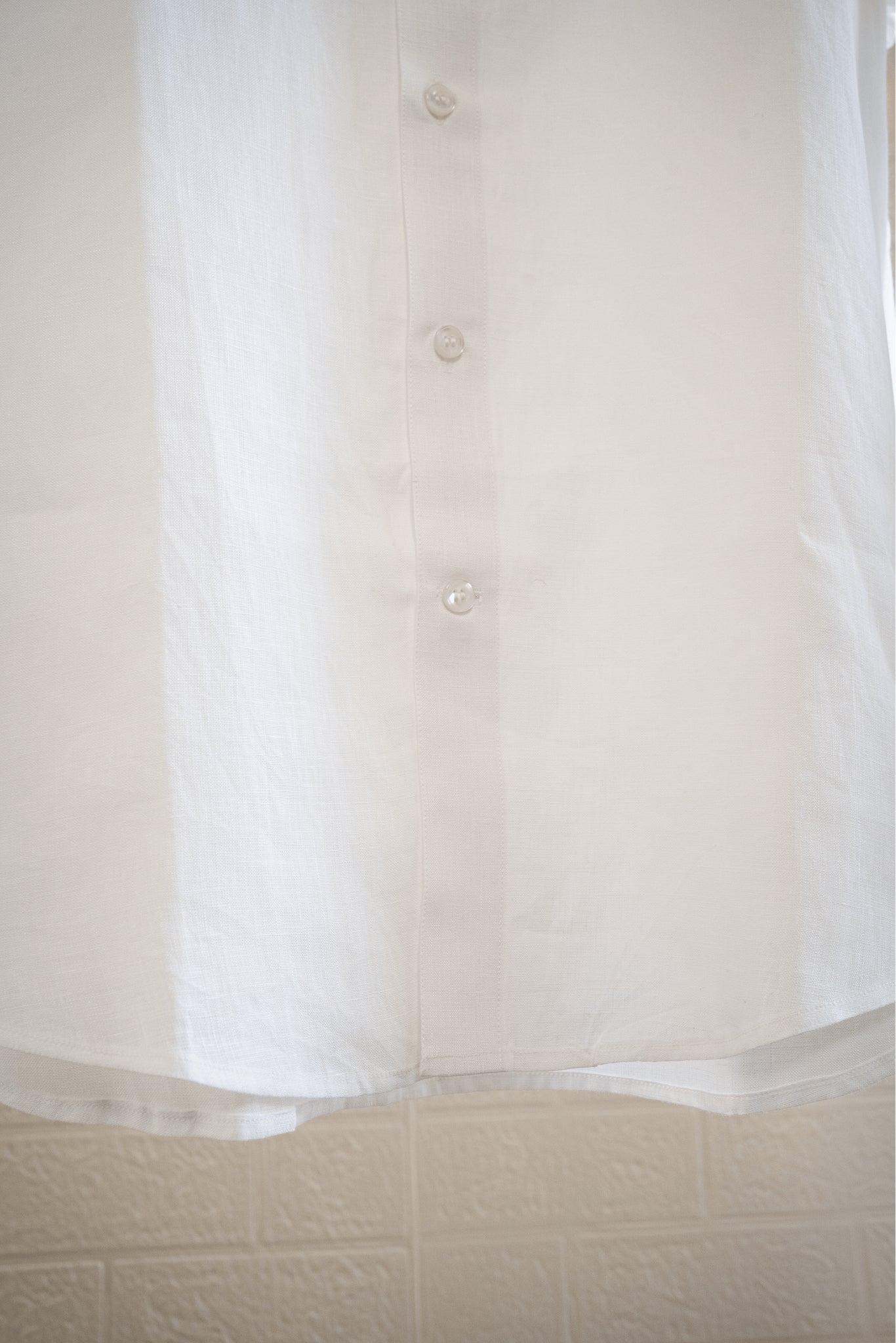 Close-up of a  chalk or white button-up shirt with a textured beige background